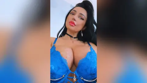 Glamorous woman in a blue lace bodysuit and black choker posing against a bright sky background.