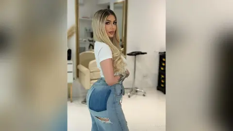 Blonde woman in white t-shirt and ripped blue jeans posing in a bright modern living room.