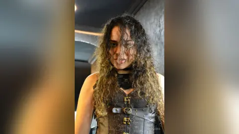 Woman with long curly hair wearing a black gothic corset in a moody indoor setting.