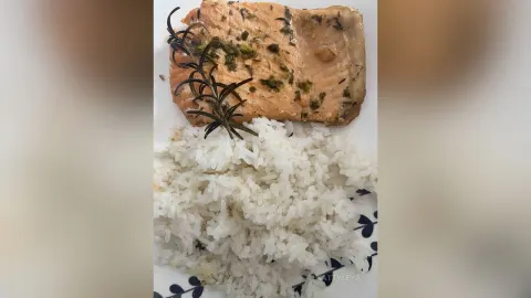 KattyLeya — KattyLeya presents a plate of cooked salmon topped with rosemary served alongside white rice.