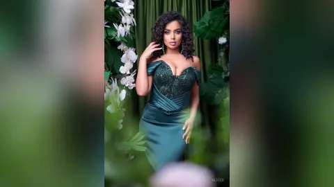 Elegant woman in a dark green sequined evening gown posing in a lush tropical garden setting.