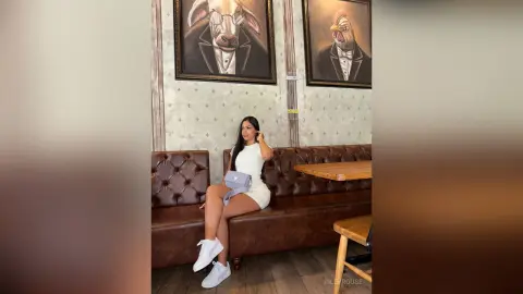 Stylish woman in a white mini dress and sneakers sitting on a leather booth in a cafe with quirky animal art.