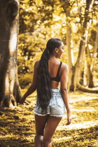 Young woman in black crop top and denim shorts standing in a sunlit golden forest.