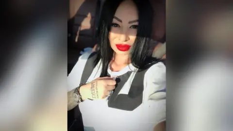 DeeaAnderson poses wearing a white t-shirt with a black graphic, showing her long black hair and bright red lipstick.