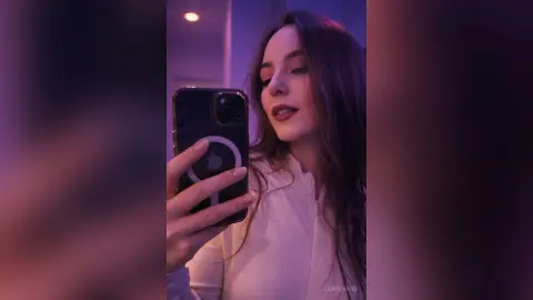 LeahEvans takes a mirror selfie wearing a white zip-up top with her long dark hair down.