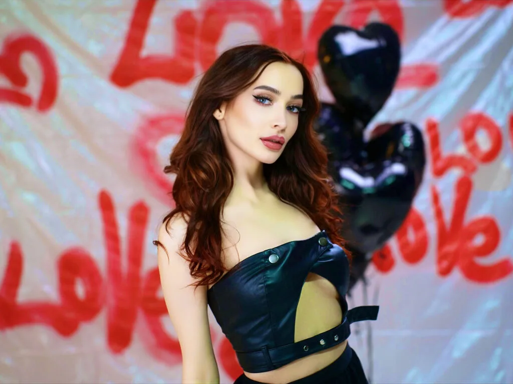 MariaBarker — MariaBarker poses in a black leather cutout top against a white background with red love graffiti and black heart balloons.