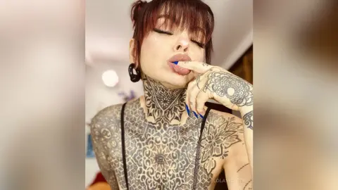 Tattooed woman with intricate black ink art posing in a casual indoor setting with a relaxed mood.