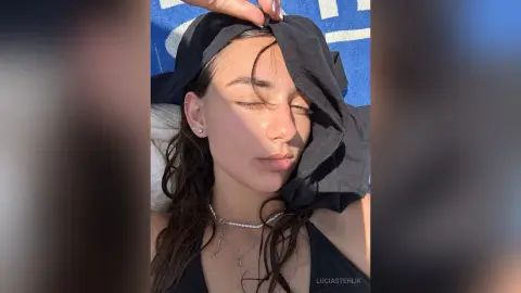 Young woman with long dark hair wearing a black top and pearl necklace relaxing in bright sunlight.