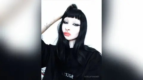 Goth girl with long black hair and heavy eyeliner wearing a black t-shirt in a minimalist moody setting.