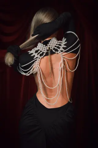 Elegant woman in a black backless dress with ornate pearl embellishments against a moody red velvet backdrop.