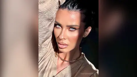 Glamorous woman with winged eyeliner and gold jewelry posing in warm sunlight.