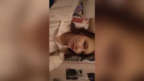 Young woman in white loungewear relaxing in a cozy bedroom setting with a peaceful mood.