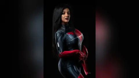 MissyJolie poses in a tight black and red latex bodysuit against a black background.