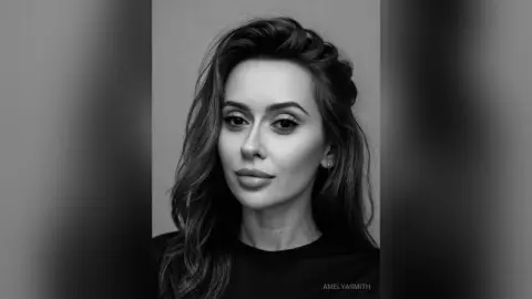 Portrait of a beautiful woman with long wavy hair looking serene in a moody black and white studio shot.
