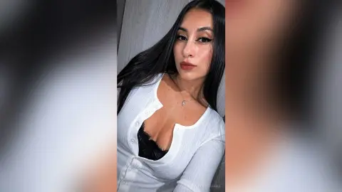 AnnyeWilliams poses in a white button-up shirt and black lace bra, looking at the camera with long dark hair.