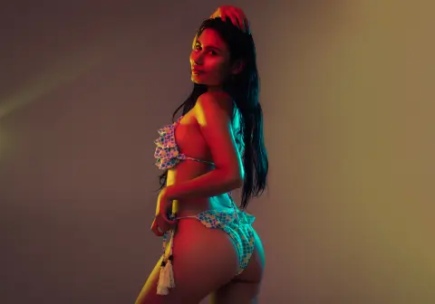 Young woman in a blue polka dot bikini posing under colorful cinematic lighting in a studio setting.