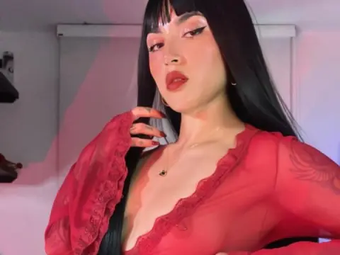 Woman with long black hair in a red sheer lace blouse posing with a moody, romantic aesthetic.