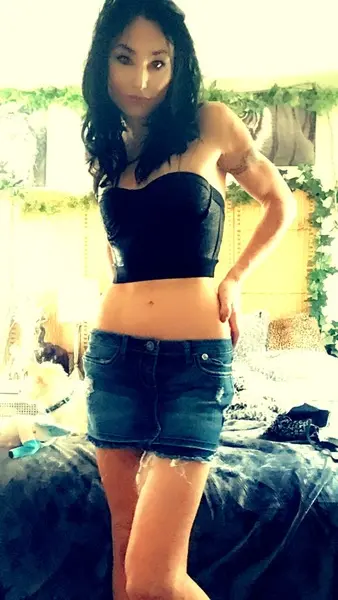 RubyLaneX poses with long dark hair, wearing a black lace bra that shows off her cleavage against a dark background.