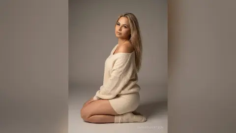 Blonde woman in a cozy cream knit sweater and matching skirt sitting against a neutral studio background.