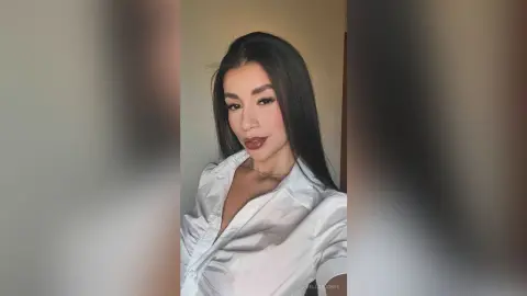 BellaaJones with long dark hair wearing a white button-down shirt looking at the camera.