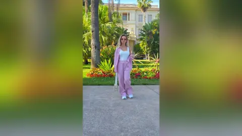 Stylish woman in a pink lounge set standing in a lush tropical garden by a luxury villa.