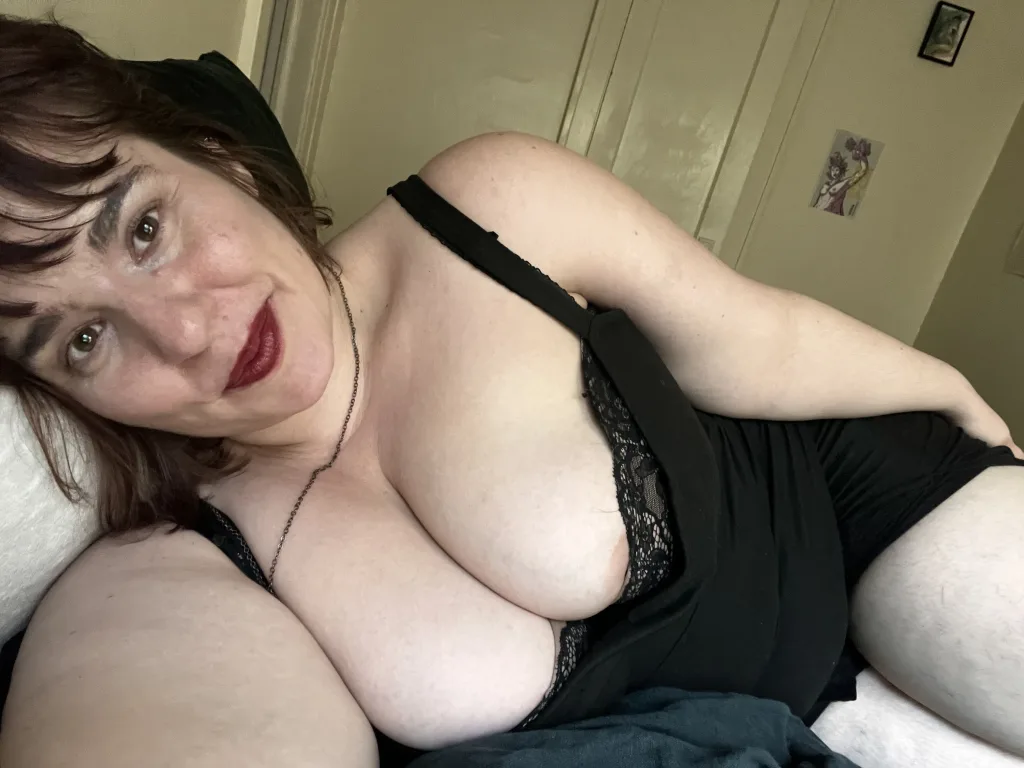 AvaCeleste looks into the camera with her red hair and dark eyes, showing her bare shoulders and chest in a close-up shot.