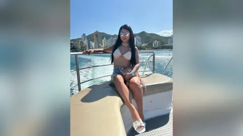 Woman in white bikini and denim shorts relaxing on a boat in a sunny tropical coastal setting.