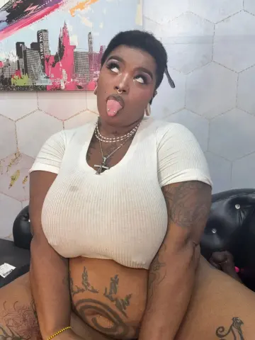Curvy woman with tattoos in a white ribbed crop top making a playful face in a modern room.