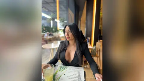 Elegant woman in a black long-sleeve bodysuit sitting at a cafe table with a refreshing drink.