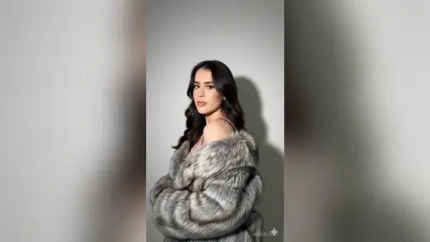 Elegant woman in a luxurious grey faux fur coat posing against a minimalist studio background.