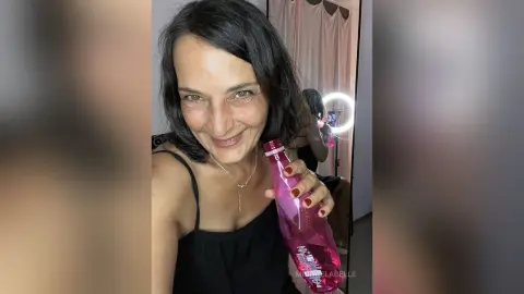 MichaelaBelle smiles while holding a pink water bottle and wearing a black tank top with a silver necklace.