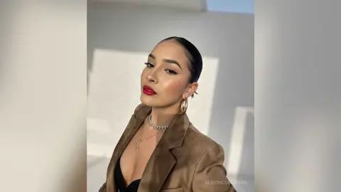 Elegant woman in a brown blazer and gold hoop earrings posing with red lipstick in soft sunlight.