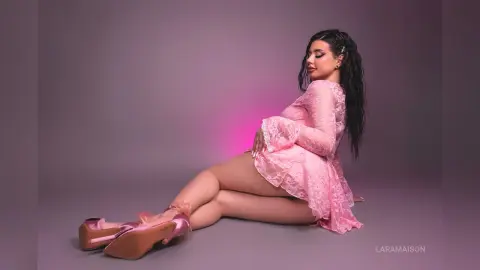 Elegant woman in a pink lace dress sitting against a soft purple background in a dreamy, romantic mood.