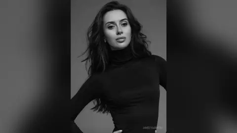 Elegant woman in a black turtleneck sweater posing for a moody black and white studio portrait.