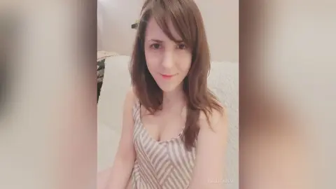 Young woman with long brown hair wearing a striped tank top in a bright, cozy indoor setting.