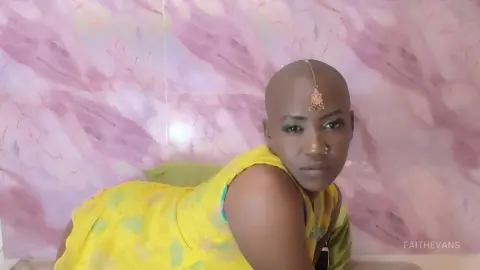 Smiling Black woman in a bright yellow traditional outfit posing against a pink marble background.