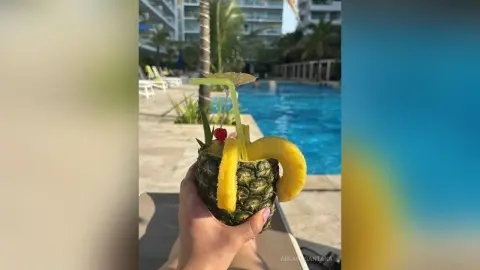 Refreshing tropical pineapple cocktail held by a hand at a sunny luxury resort swimming pool.