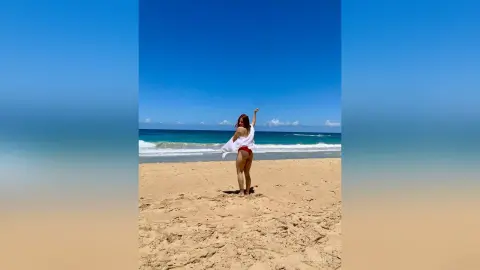 Woman in white cover-up and red bikini enjoying a sunny day on a sandy tropical beach.