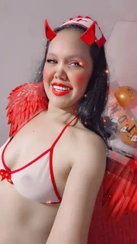 Smiling woman in a white and red angel costume with red wings and headband in a bright indoor setting.