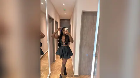 Stylish young woman in a black crop top and mini skirt taking a mirror selfie in a modern hallway.