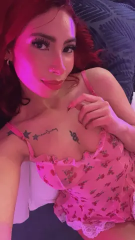 Woman in pink floral lace camisole relaxing in moody pink lighting.