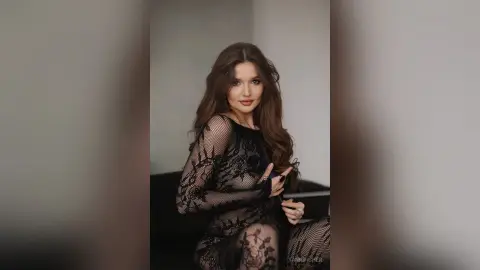 Elegant woman in a black lace long-sleeve dress posing with a moody, sophisticated look in a minimalist setting.