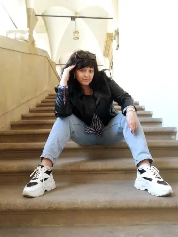 Polunichka039 sits on stone stairs wearing a black leather jacket, blue jeans, and white sneakers.