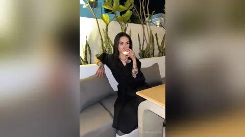 Stylish woman in a black dress sipping a drink on a modern patio at night.