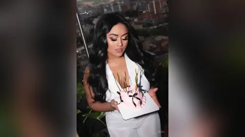 Glamorous woman in a white outfit holding a pink cake on a rooftop balcony at night.