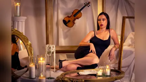 Elegant woman in a black dress sitting in a dreamy, candlelit room surrounded by vintage gold mirrors.
