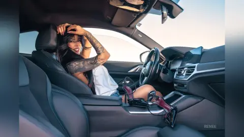 Tattooed woman in a white top relaxing in a luxury car interior during a bright, sunny day.