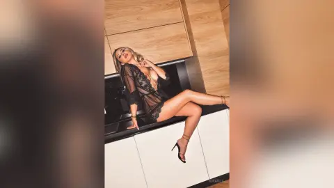 Glamorous blonde woman in a black lace sheer negligee sitting on a modern kitchen counter.