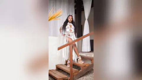 Stylish woman in a white crochet cutout maxi dress posing on wooden stairs in a bright, airy summer setting.