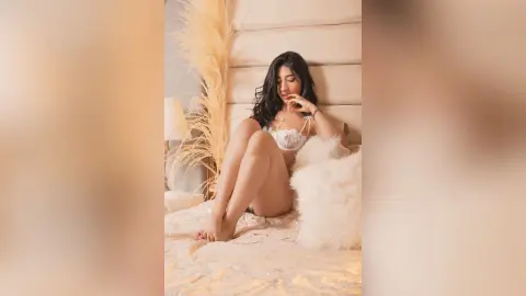 Young woman in white lace lingerie relaxing on a cozy bed in a warm, aesthetic bedroom setting.